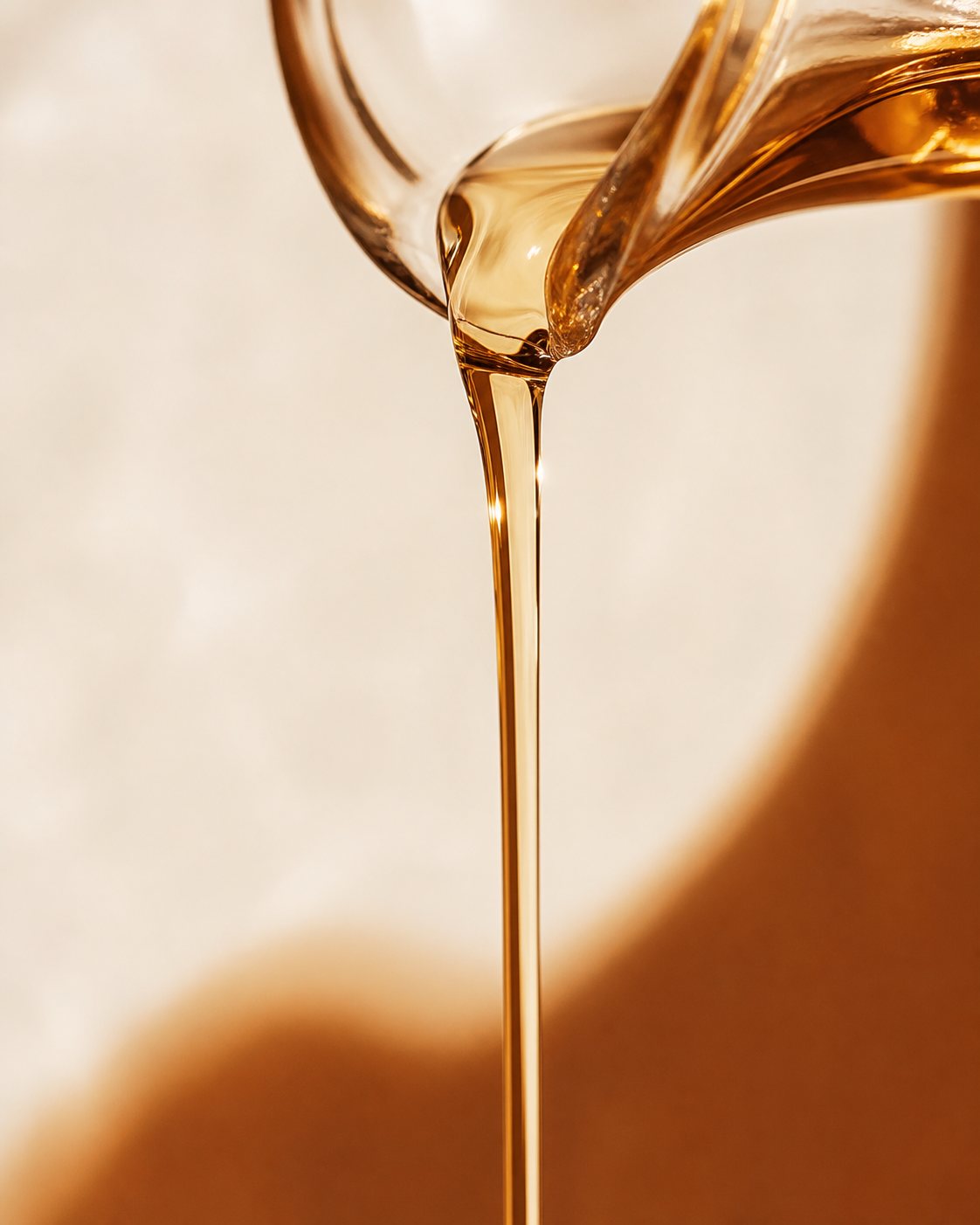 Golden massage oil pouring in a thin ribbon, warm light